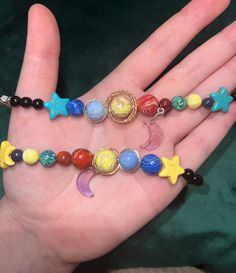 the hand is holding several bracelets with beads and charms on them, including an astrological star