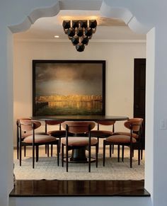 a dining room table with chairs and a painting on the wall behind it in an archway