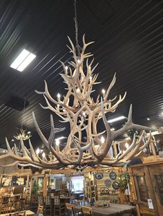 a large antler chandelier hanging from the ceiling in a store filled with tables and chairs