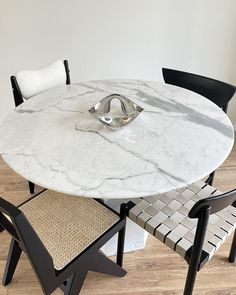 a marble dining table with two chairs and a bowl on the top, in front of a white wall