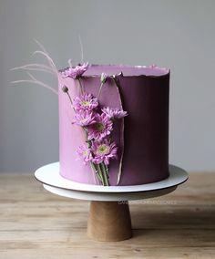 a purple cake with pink flowers on top sitting on a white plate next to a wooden table