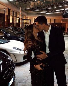 a man and woman kissing in front of some cars