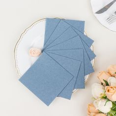 place setting with blue napkins and flowers on white table cloth next to silverware