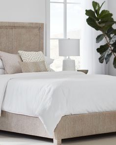 a bed with white linens and pillows in a bedroom next to a plant on the floor