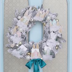 a christmas wreath with white and silver decorations on the front, hanging from a blue door