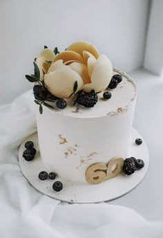 a three tiered cake decorated with berries and leaves on a white tablecloth background