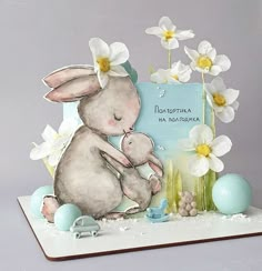 a card with an image of a bunny holding a baby in its lap, surrounded by flowers and eggs