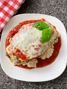 a white plate topped with lasagna covered in sauce and garnished with green leaves