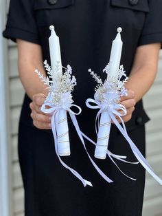 two white candles with flowers and ribbons in their hands