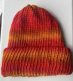 an orange and yellow knitted beanie sitting on top of a white boarder