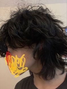 a man with long black hair has yellow graffiti on his face and is looking to the side