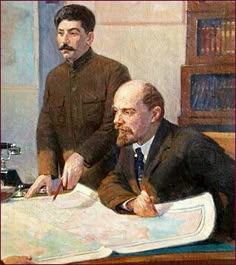 two men are sitting at a table with papers and pens in front of them, one is looking at the viewer