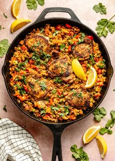 a skillet filled with chicken and rice next to lemon wedges on a table