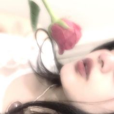 a woman laying on top of a bed next to a red rose in her hair