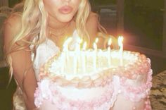 a blonde woman sitting in front of a cake with lit candles on top of it