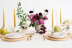 a white table topped with plates and vases filled with flowers next to tall candles