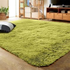 a green rug with black and white pillows on the floor in front of a television