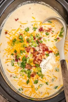 a bowl of soup with cheese, bacon and green onions in it next to a spoon