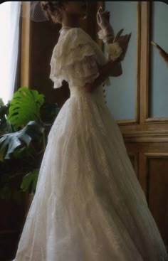 a woman in a white dress is standing by a window