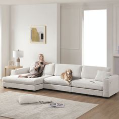 a woman sitting on top of a white couch next to a brown dog in a living room