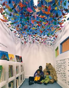 two children sitting on the floor in front of bookshelves with origami birds hanging from the ceiling