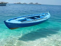 a small blue boat floating on top of the ocean next to a shore line with boats in the background