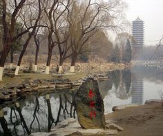 a body of water surrounded by trees, rocks and pagodas in the background on a foggy day