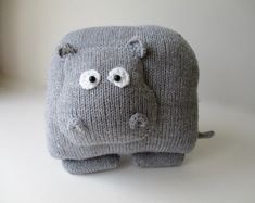 a gray knitted hippo stuffed animal with big eyes and ears, sitting on a white surface