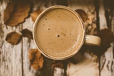 a cup of coffee sitting on top of a wooden table next to leaves and nuts