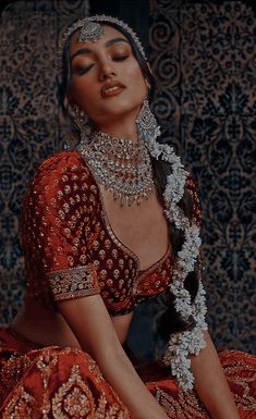 a woman in a red and gold dress with jewelry on her neck, sitting down