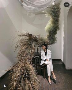 a woman sitting on top of a bench next to a tall plant in a room