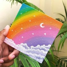 someone is holding up a small card with a rainbow painted on it and stars in the sky