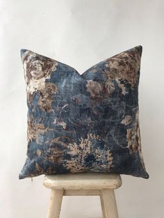 a blue and brown floral pillow sitting on top of a wooden stool next to a white wall