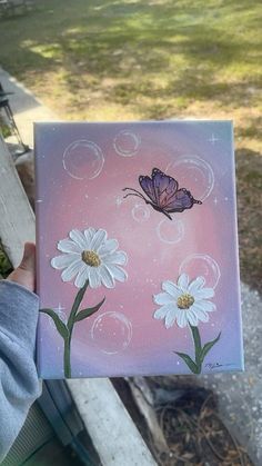 a person holding up a painting with daisies and a butterfly on it