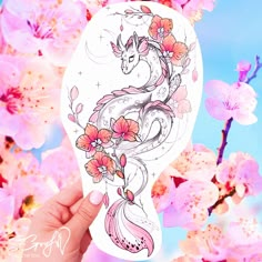 a hand holding up a sticker with flowers and a dragon on it's face