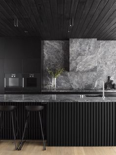 a kitchen with black cabinets and marble counter tops, two stools in front of the sink