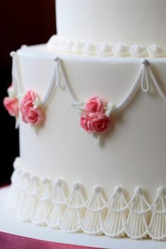 a three tiered white cake with pink flowers on the icing and lace decoration