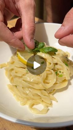 two hands picking up a slice of lemon from a plate of pasta