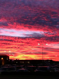 a parking lot filled with lots of parked cars under a colorful sky at night time