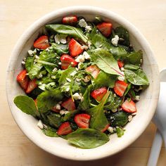 a salad with spinach, strawberries and feta cheese in a white bowl