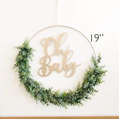 a wooden sign that says oh baby hanging on a wall with greenery around it