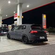 two cars are parked in front of a gas station with people standing around them at night