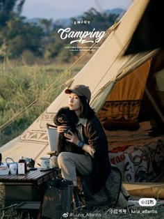 a woman sitting in front of a tent holding a dog