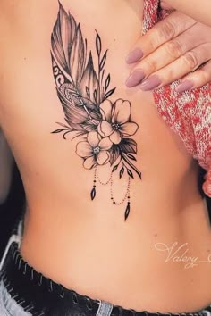 a woman's stomach with a feather and flower tattoo