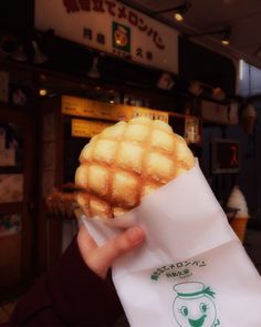 a person holding up a waffle in front of a storefront with japanese writing on it