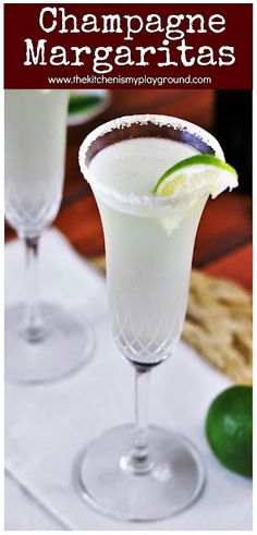 two margaritas sitting on top of a table next to limes