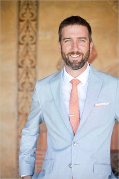 a man with a beard wearing a blue suit and orange tie smiling at the camera