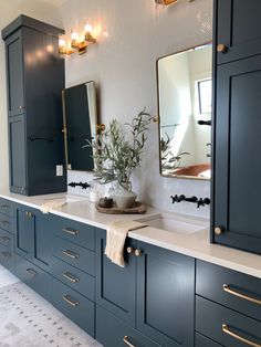 a bathroom with blue cabinets and white counter tops, gold pulls on the mirror above the sink