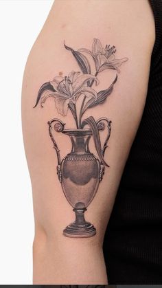 a black and white photo of a vase with flowers on the side of a woman's arm