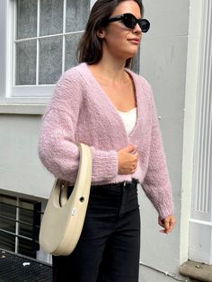 a woman in black pants and a pink cardigan sweater carrying a beige handbag